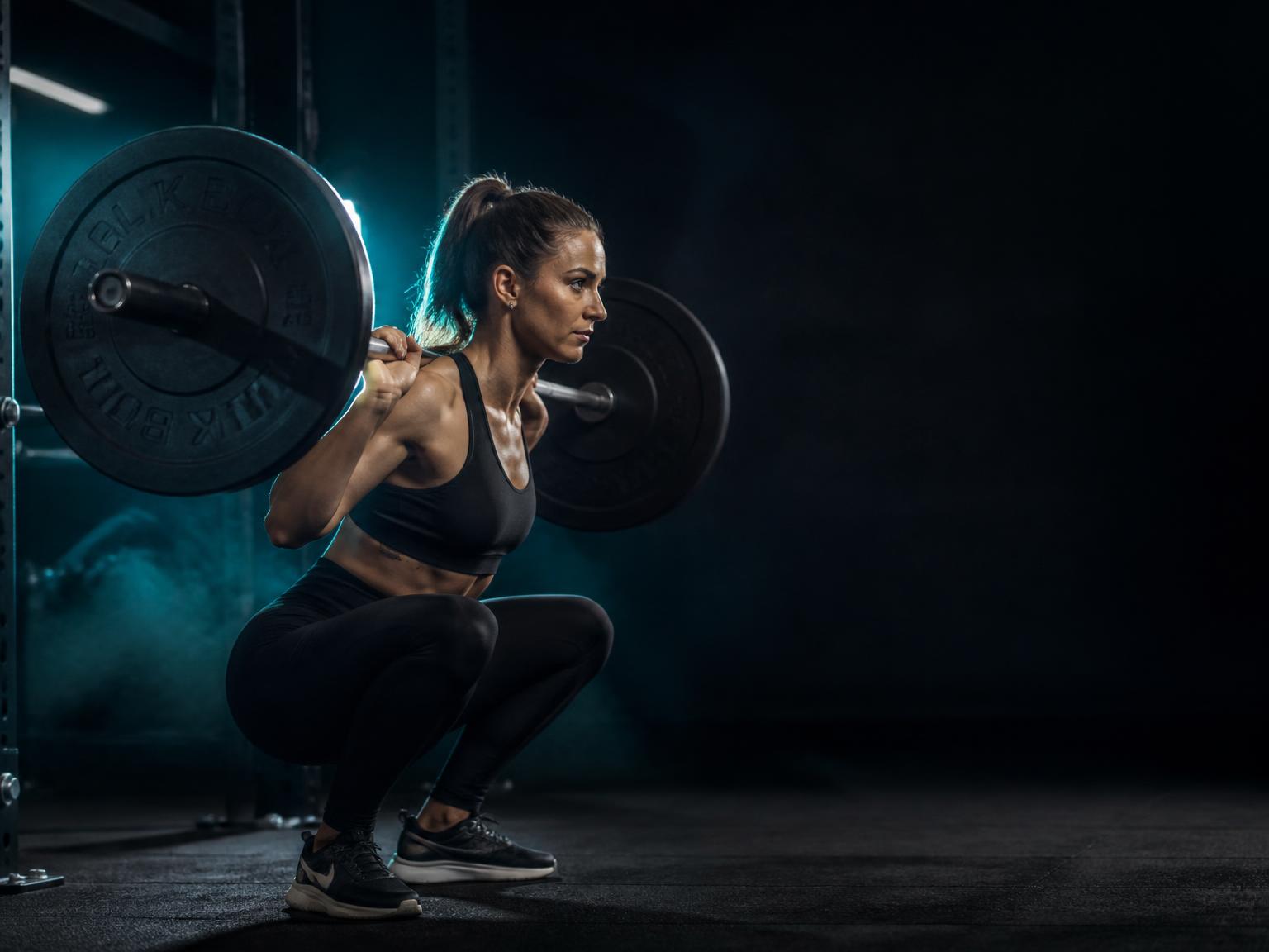 Athlete performing a barbell back squat with correct depth under cyan rim lighting